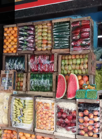 Puesto de frutas y verduras de Carolina, cajones de madera con naranjas, manzanas, morrones y sandía